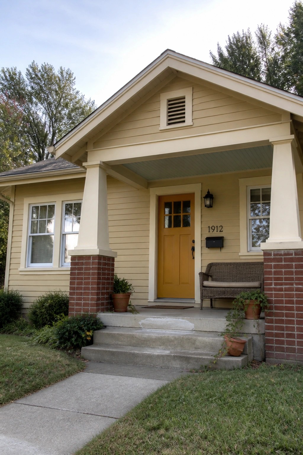 A small house exterior with pale yellow siding, red brick porch columns, and a yellow front door.