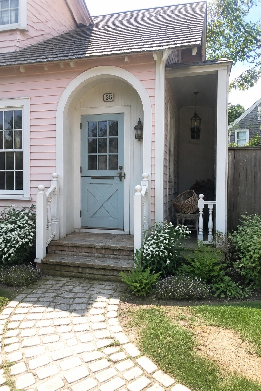 Pink house with light blue door under white arch, cobblestone path, and flowers.