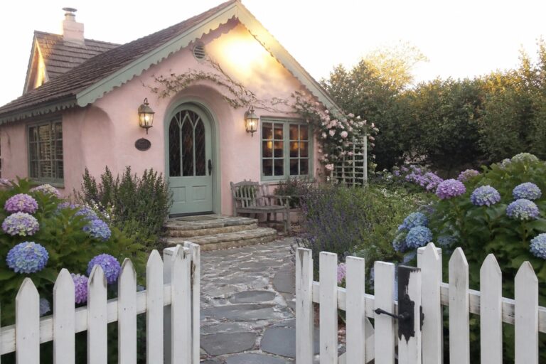 Pink cottage with green door, stone path, white fence, and blooming hydrangeas