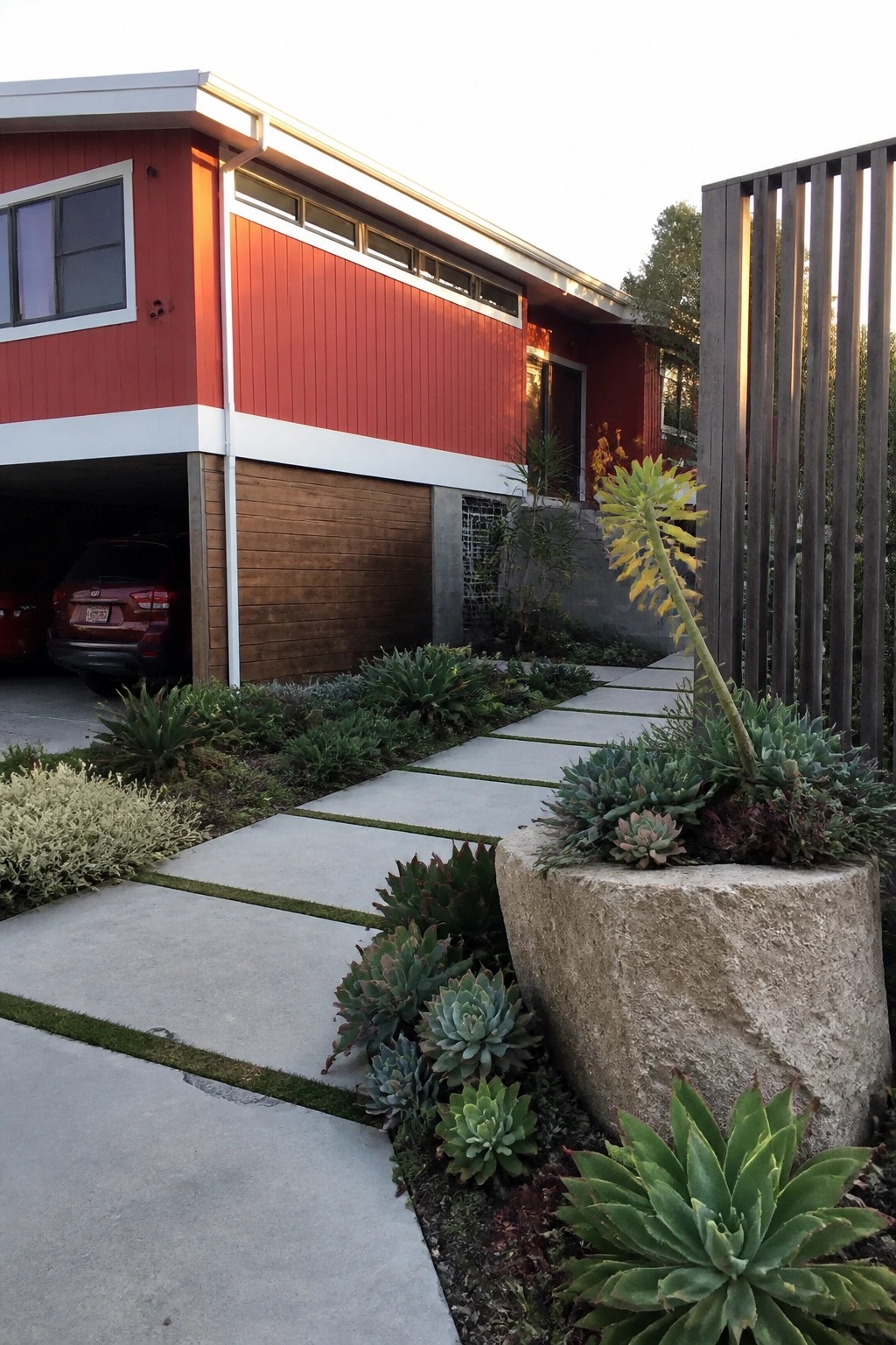 Modern red house with succulent garden, stone path, and wooden fence
