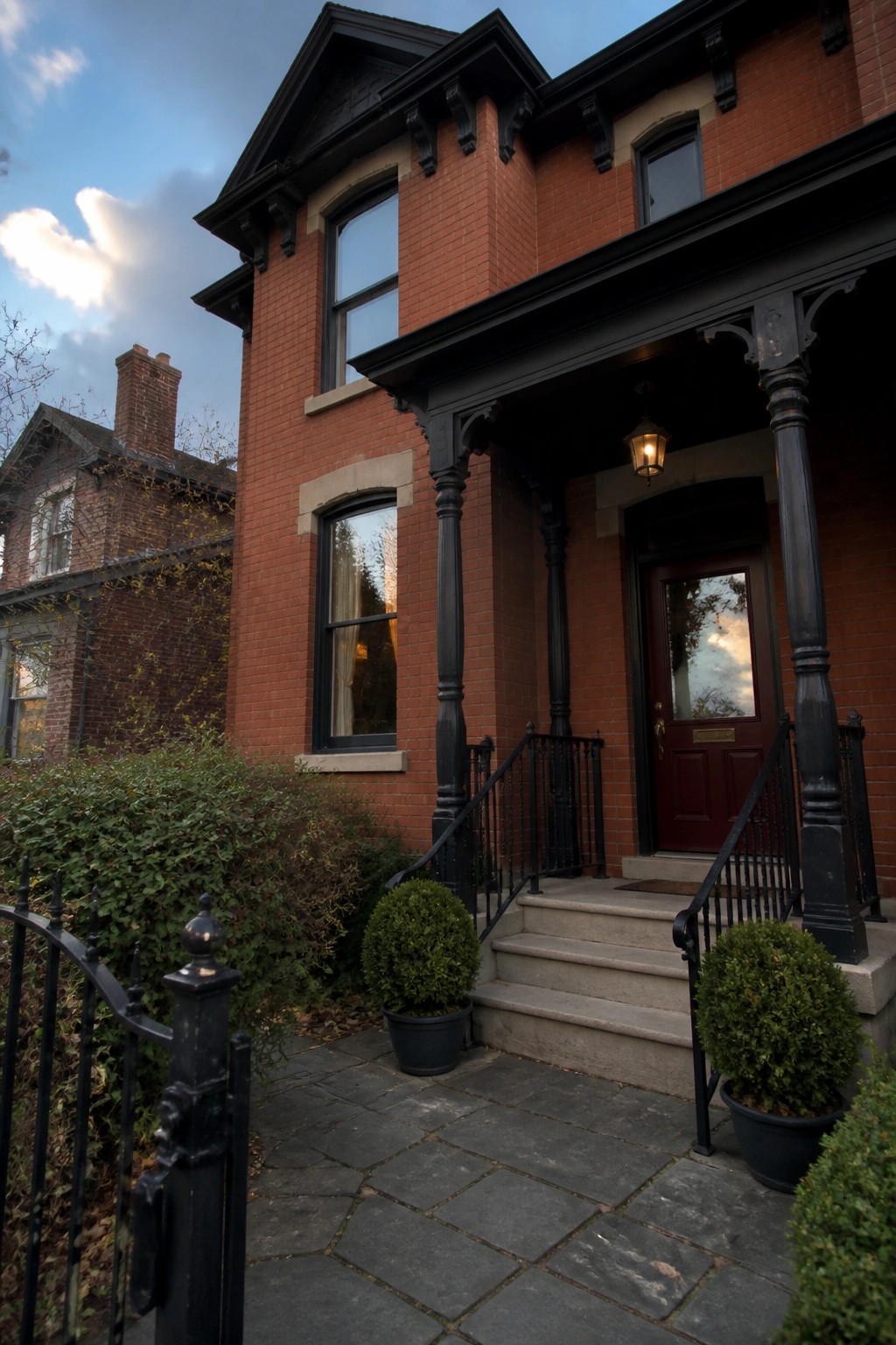 A red brick home featuring black painted trim, porch columns, and railings.