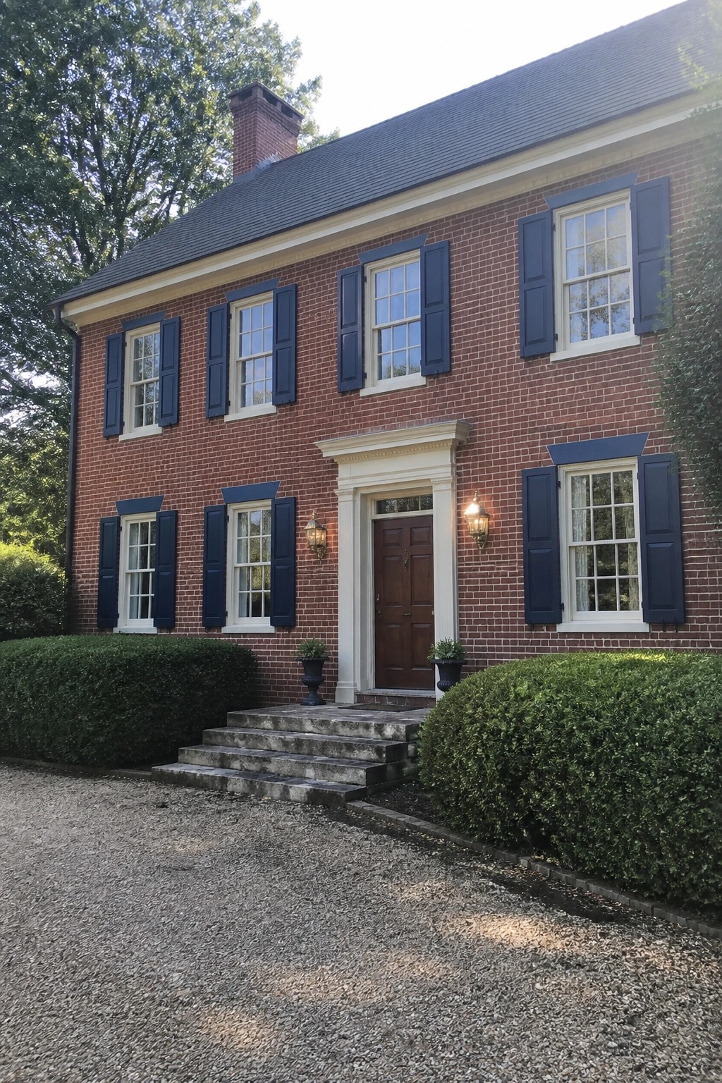 Two-story red brick house with navy shutters, white trim, and stone steps.