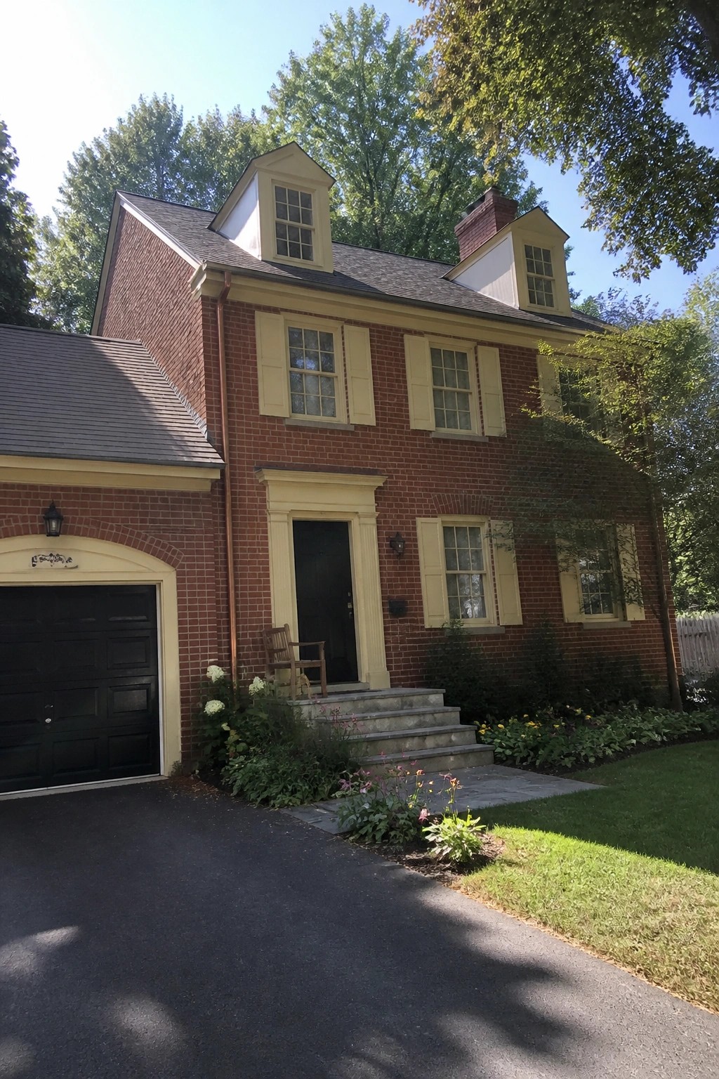 Red brick two-story house with yellow trim, dormers, and flower garden