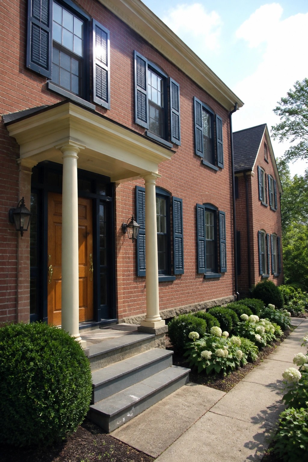 Red brick house with white columns, blue shutters, wooden door, and flower garden path