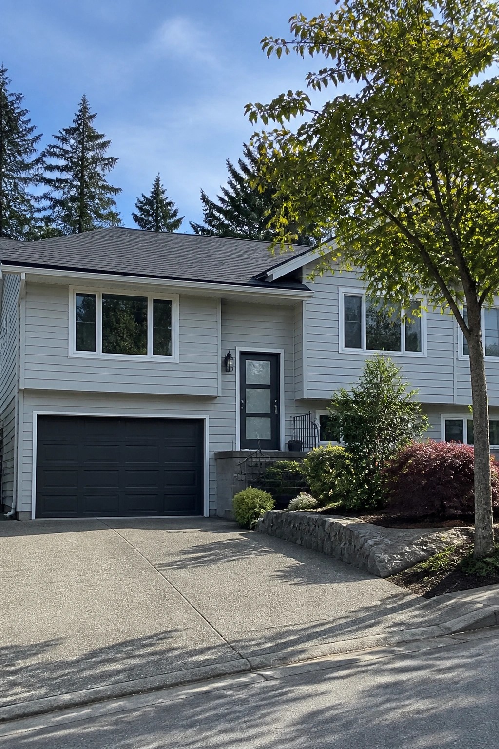 Light gray house siding on a two-story home with a dark garage door and stone landscaping.