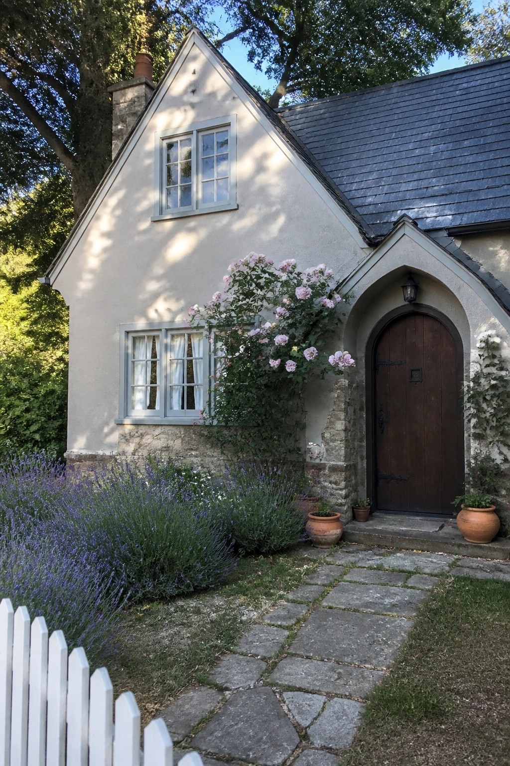 Charming stone cottage with pink roses, lavender garden, stone path, and arched door