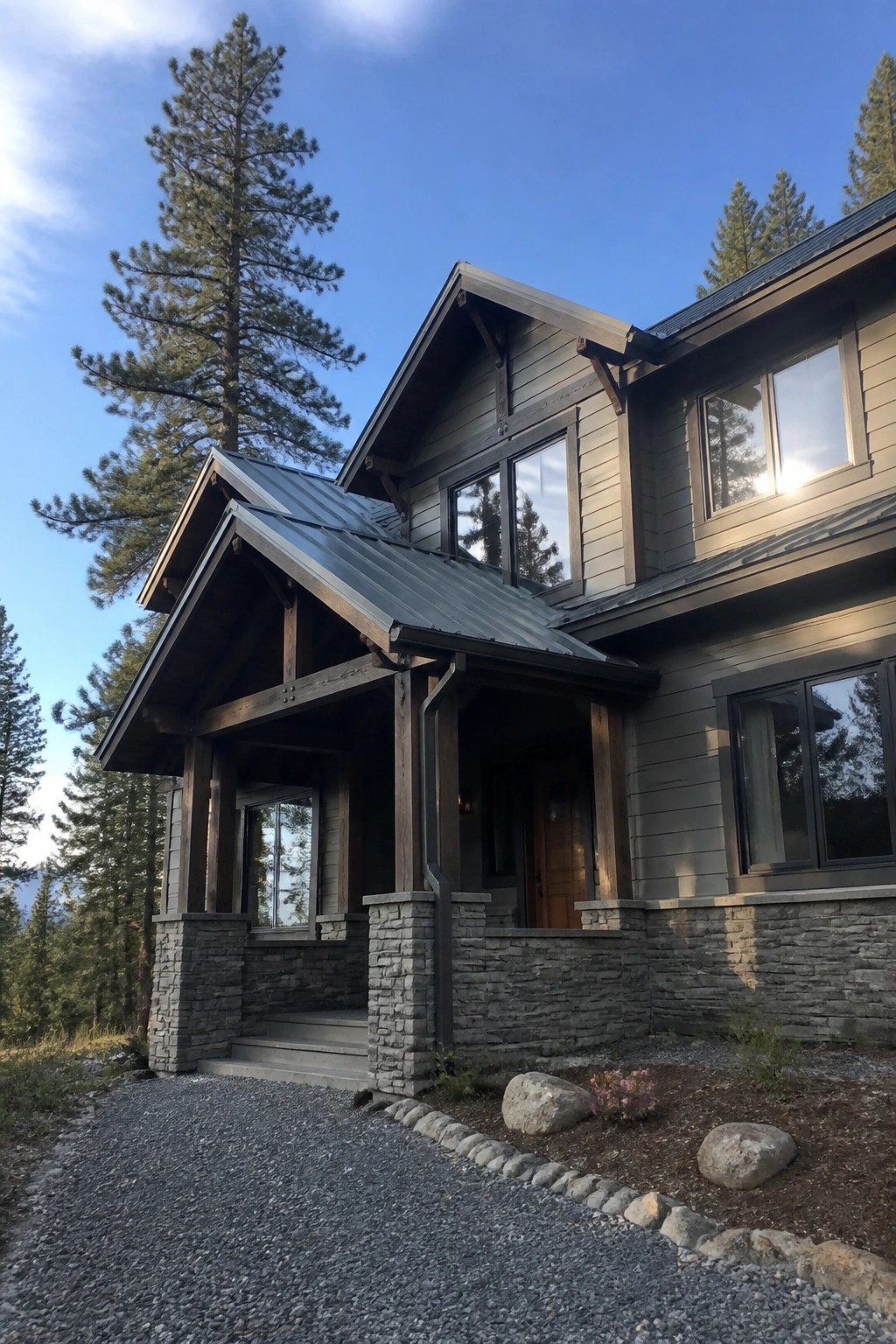 Modern gray wooden house with stone foundation, porch, and tall pine trees nearby