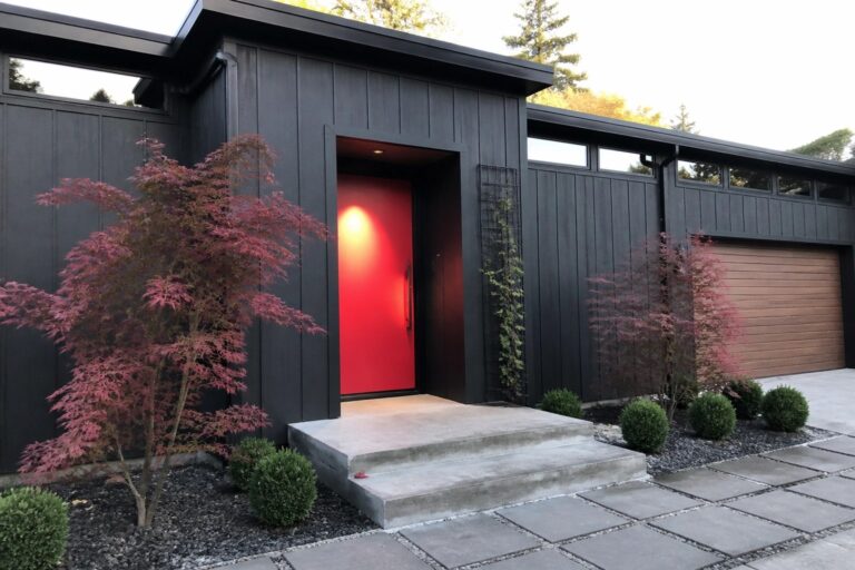 21 Striking Red and Black House Exteriors for High-Contrast Curb Appeal Modern house exterior with black siding, a bright red front door, concrete steps, and red foliage plants beside the entry.