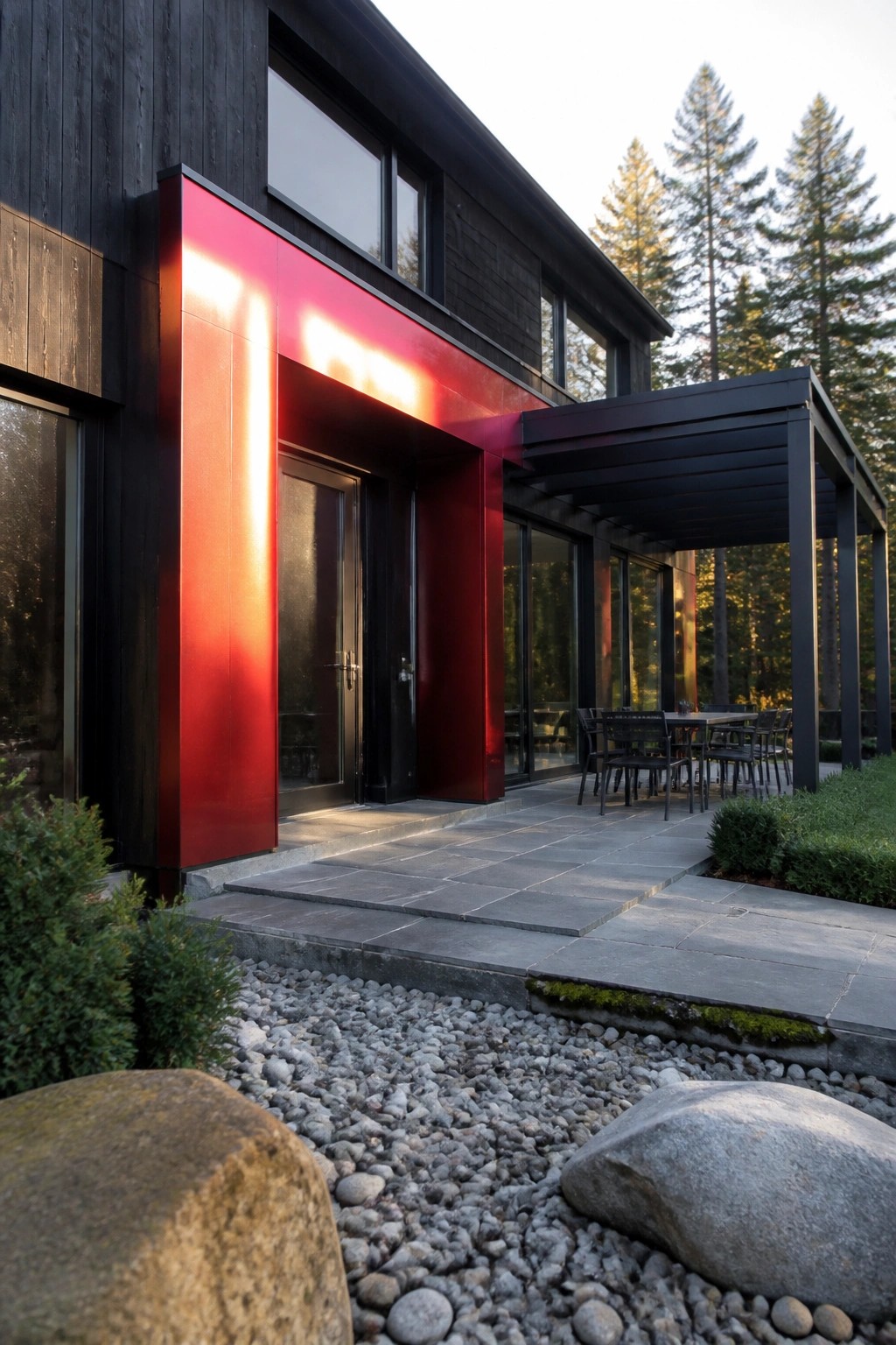 Modern house with bold red entry, black doors, stone patio, and pine trees.
