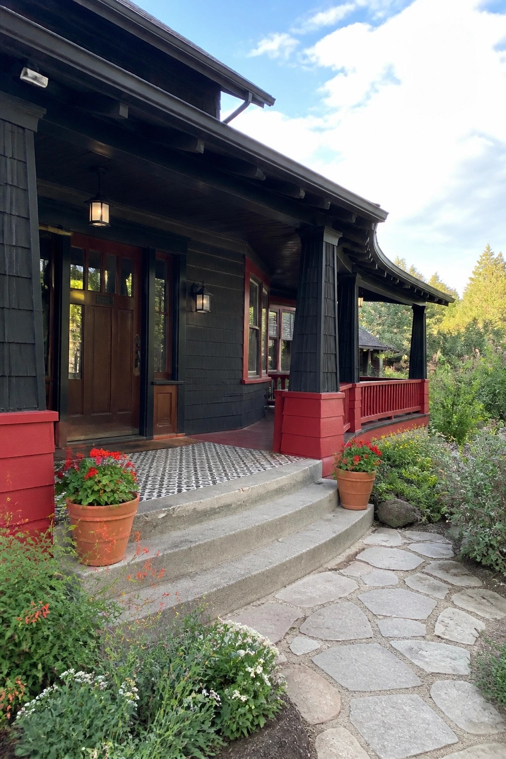 A house exterior with black siding, red-painted porch columns and railing, concrete steps, and a stone pathway.