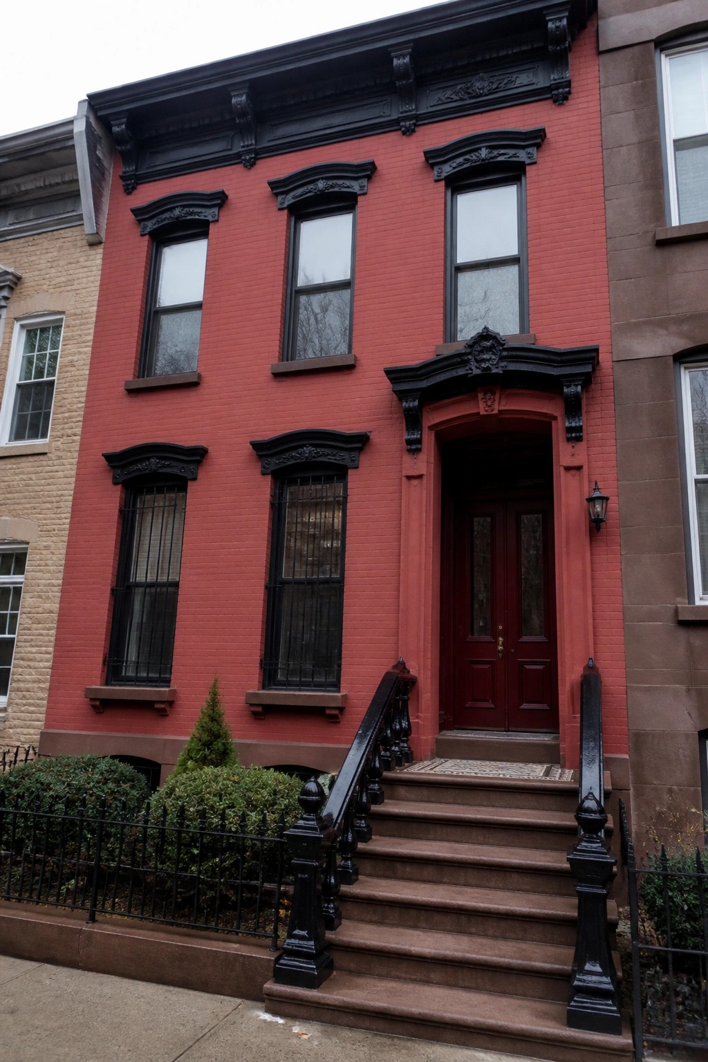 Red brick rowhouse with ornate black trim, red door, and stone staircase