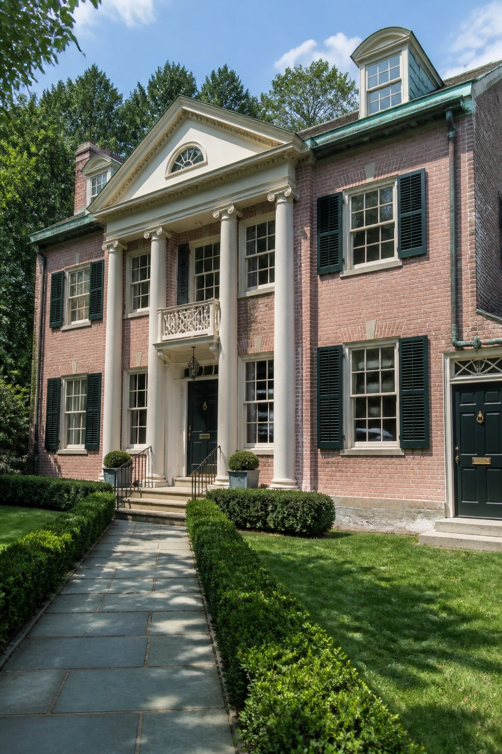 Red brick mansion with white columns, green shutters, and stone pathway to entrance