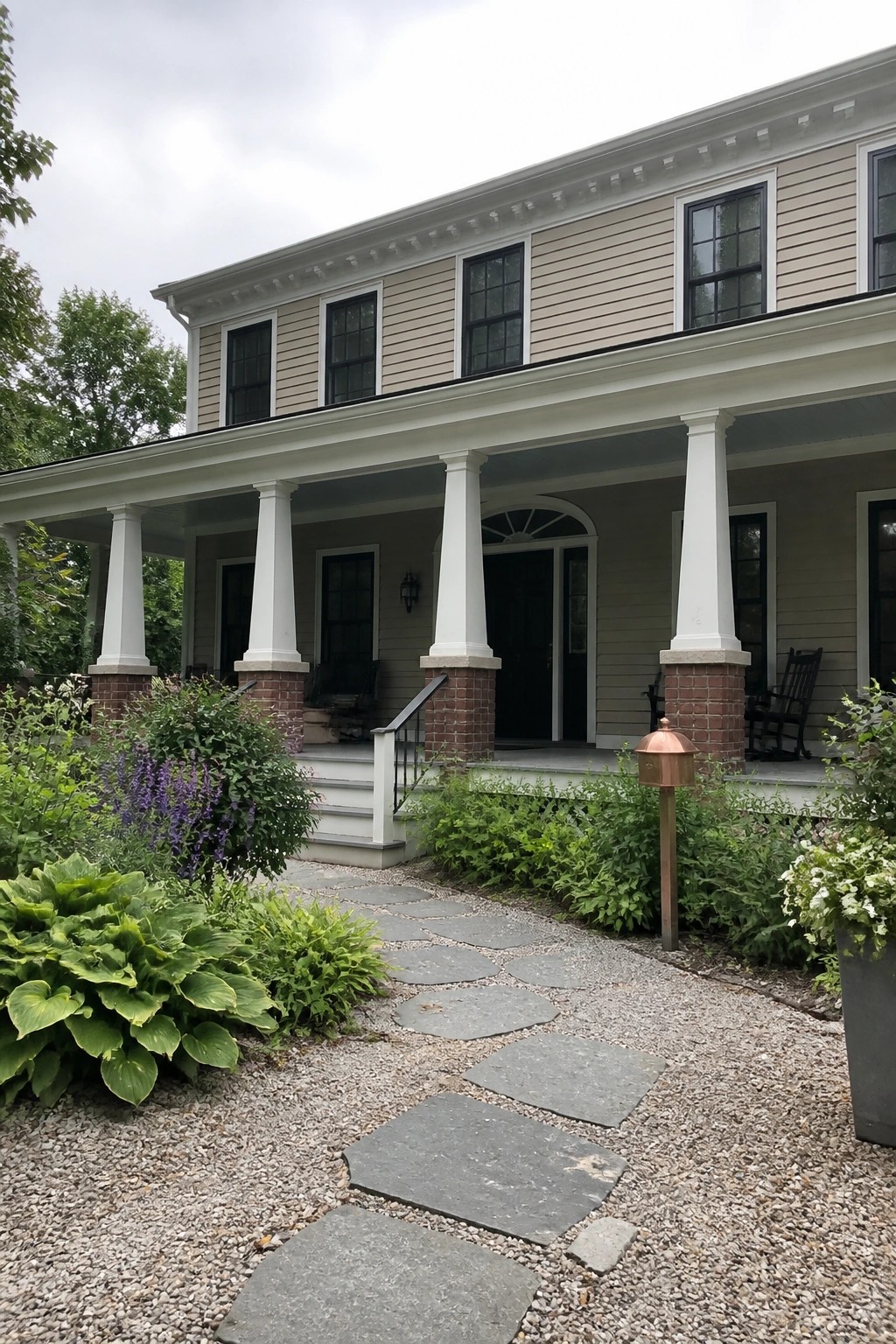 Stone pathway winds through garden to porch with white columns on two-story house.