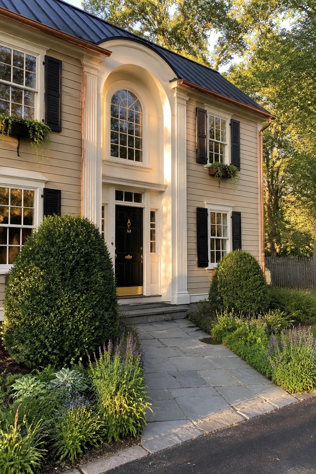 Two-story beige house with white columns, arched window, black door and stone path
