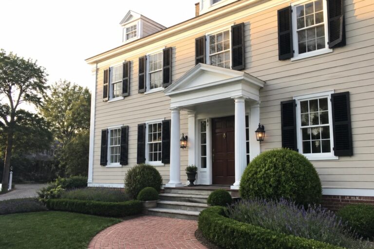 Yellow colonial house with black shutters, white columns, and brick walkway amid greenery