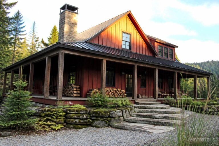 19 Cozy Red Cabin Exteriors Made for Forest and Mountain Settings Red wooden cabin with porch, rocking chairs, stone chimney amid pine trees and rocks