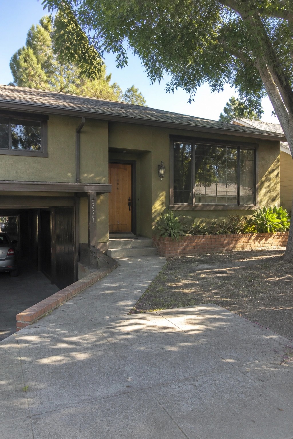 Sage green house with wooden door, garage, large window, and brick planter.