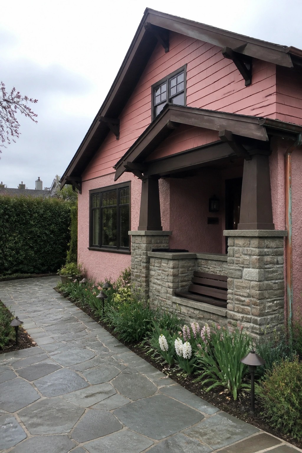 Pink house with stone porch, wooden bench, dark trim, and flower-lined pathway.