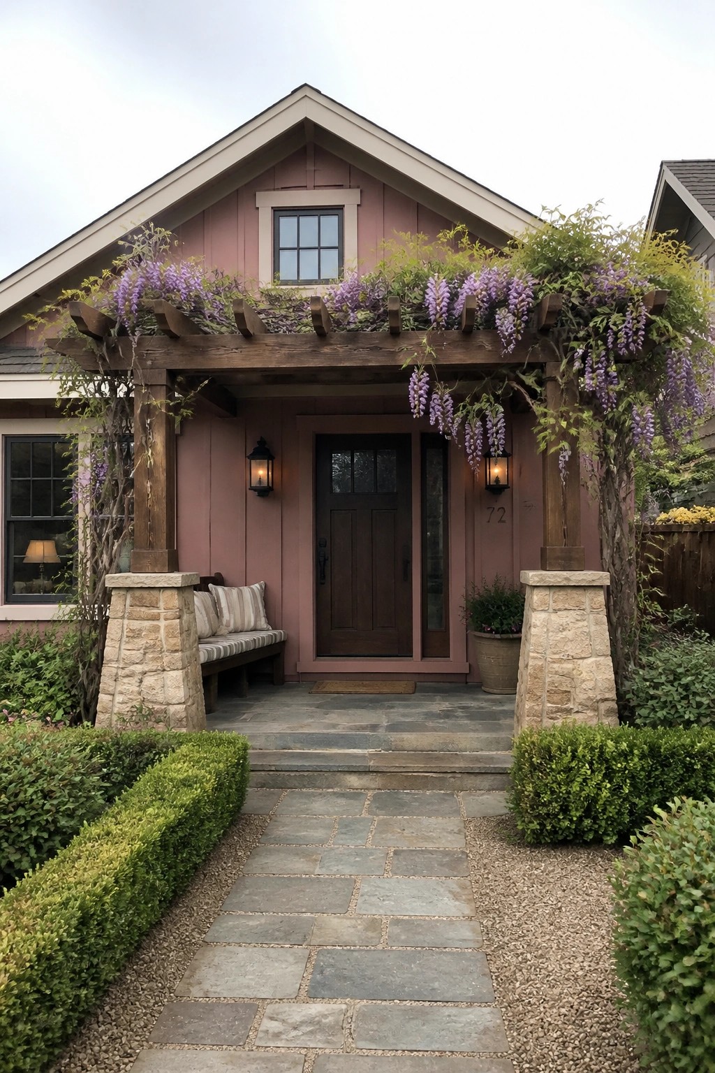 Front view of a pink Craftsman house with dark wood trim, a covered entry porch supported by stone pillars, and a central dark wood door.