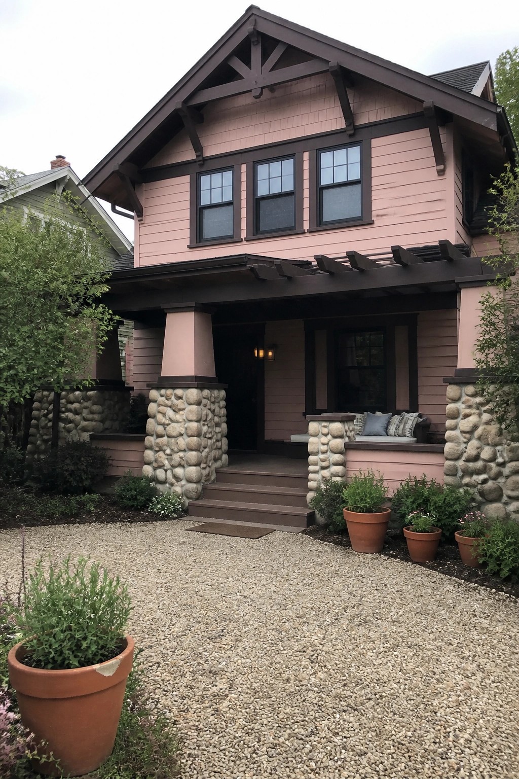 Pink two-story house with dark trim, stone columns, and gravel front yard