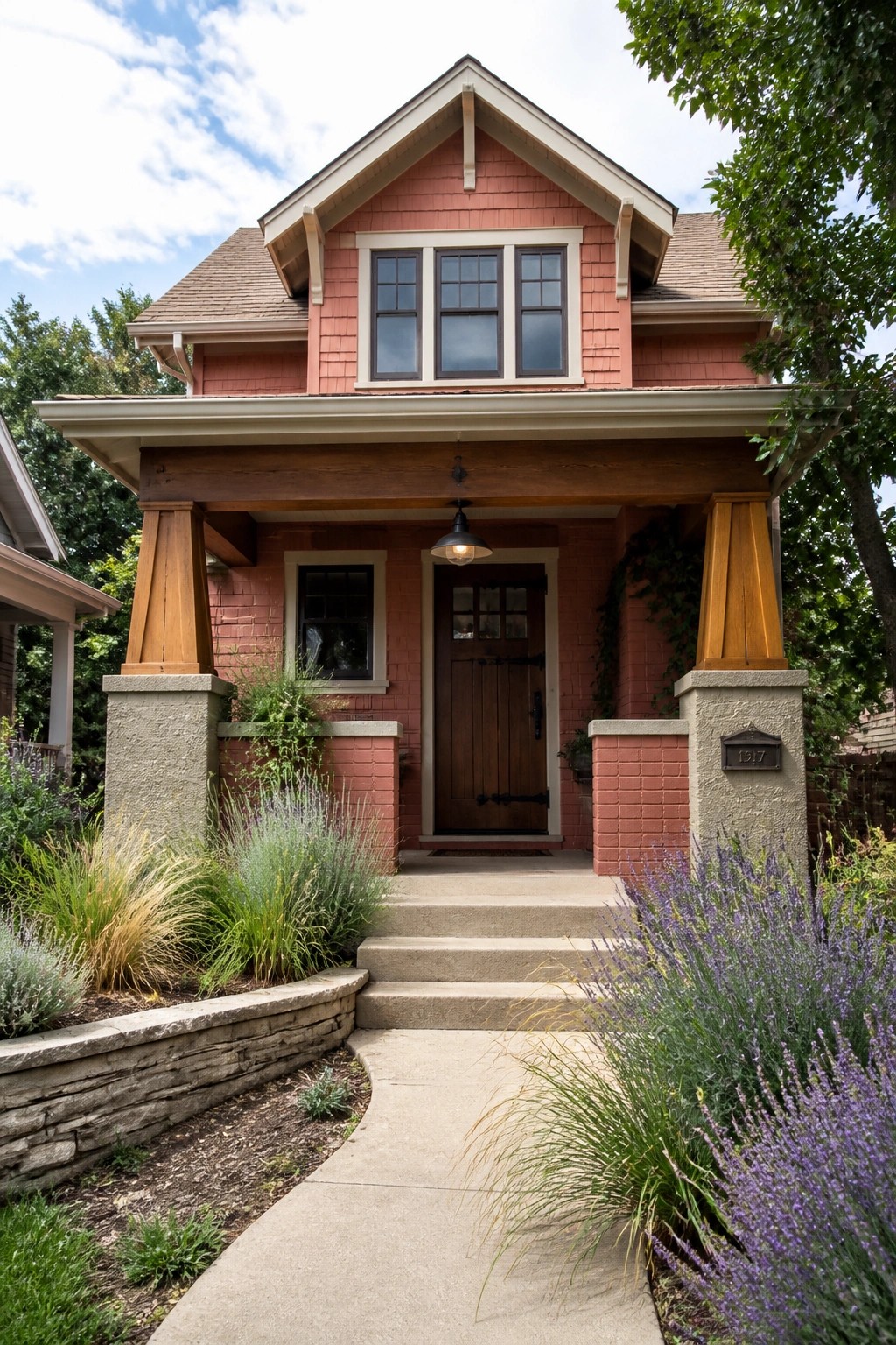Front view of a pink Craftsman house showing a covered porch with wooden posts resting on masonry piers and concrete steps leading to the front door.