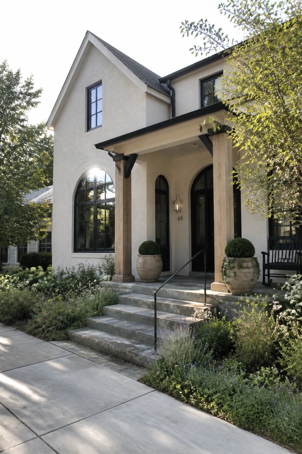Beige two-story house with arched windows, stone steps, and potted shrubs.