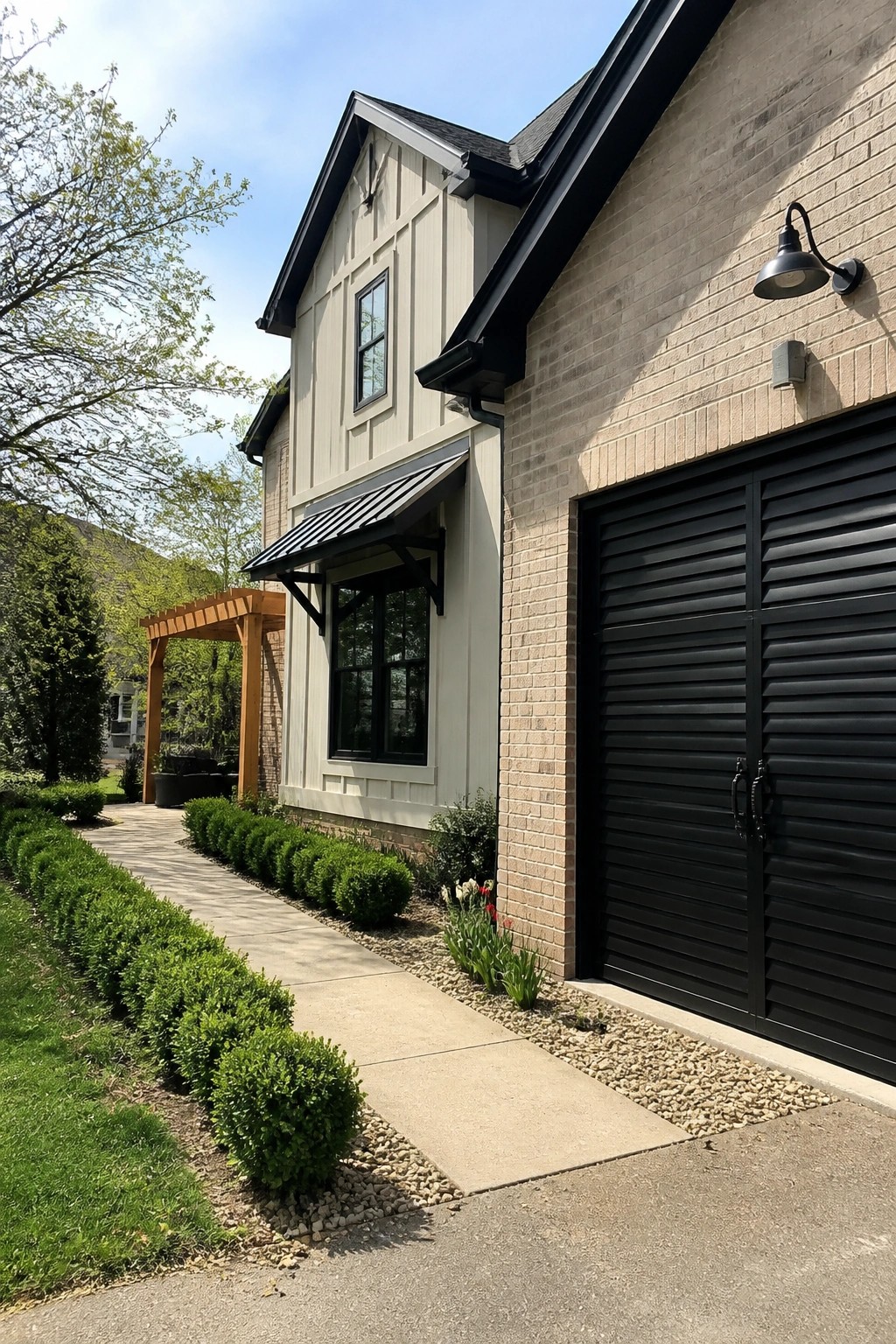 A two-story house exterior with beige siding, brick accents, black garage door, black window frames, and a black awning over one window.