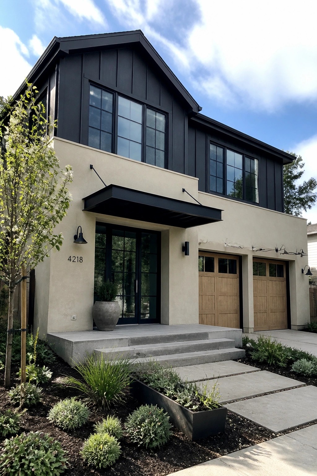 A two story house with black upper siding, beige lower walls, black framed windows and doors, a flat black entry overhang, two wooden garage doors, and a concrete front step with landscaping.