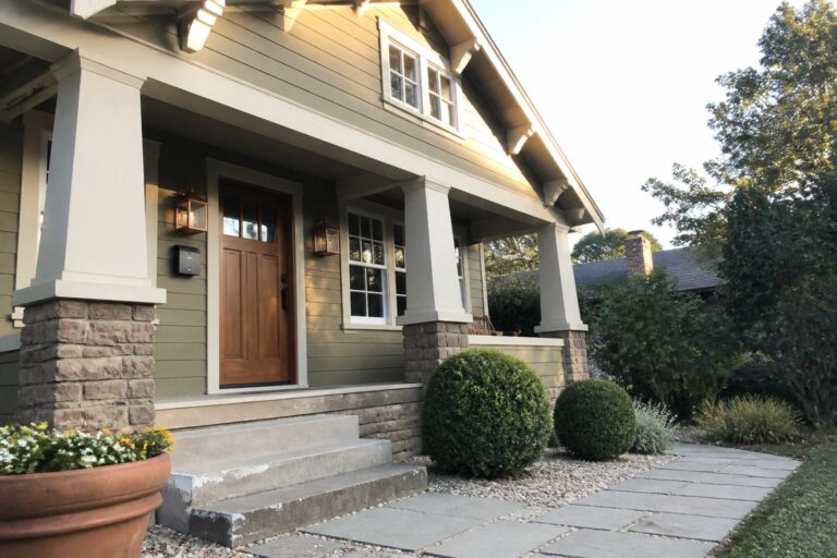 Craftsman house exterior with muted sage green siding, white trim, and stone columns.