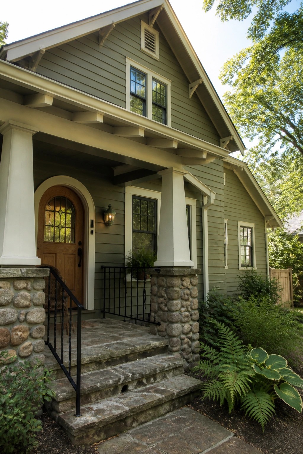 Green house with stone porch steps, white columns, arched wooden door and plants