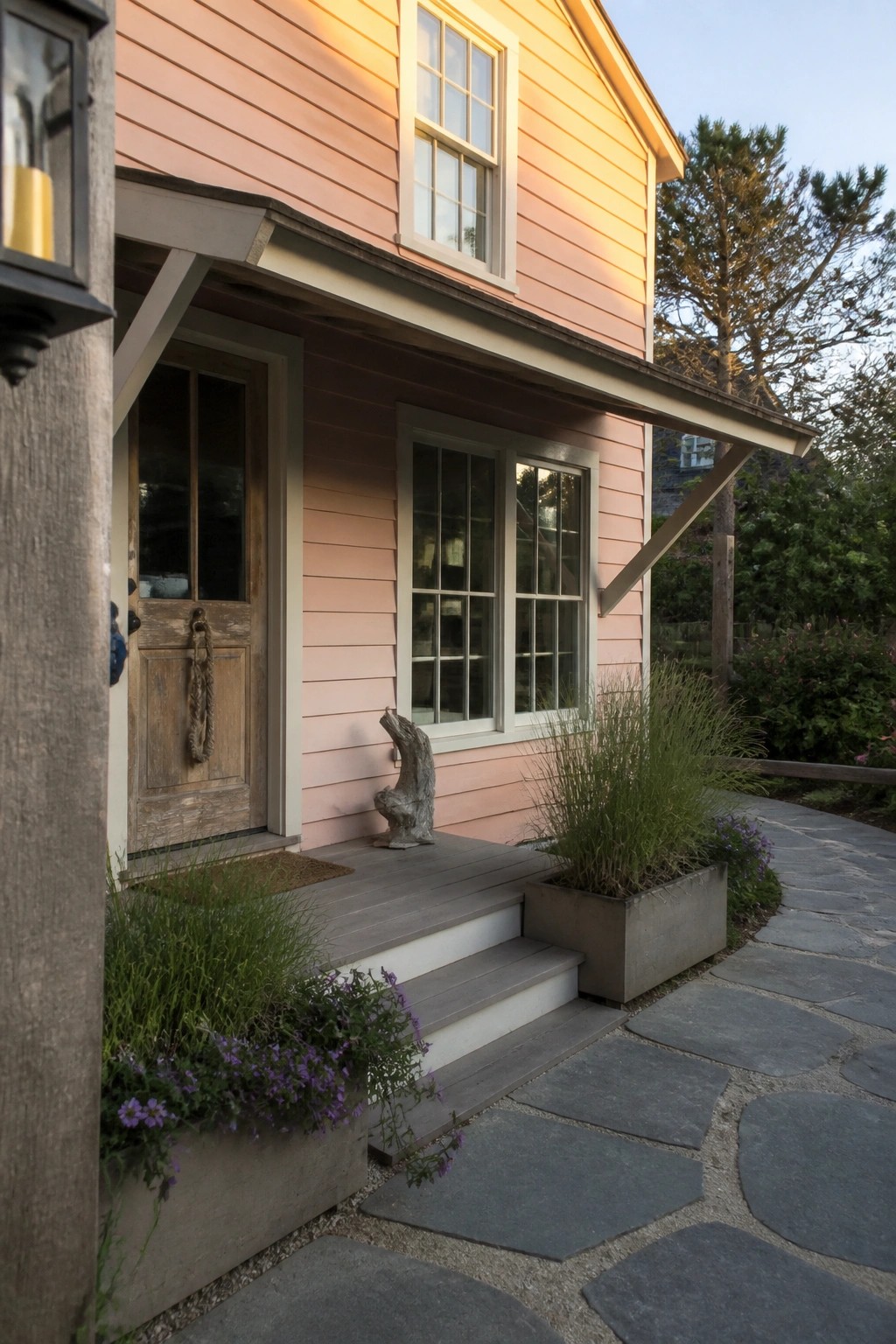 Front view of a pink wooden house with a weathered door, gray steps, concrete planters, and a stone path.