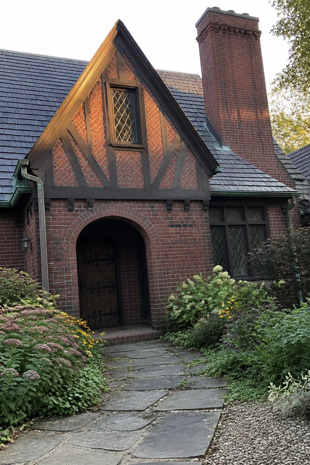 Front view of a red brick Tudor-style house with a large arched brick entry framing a wooden door and dark timber framing on the gable above.