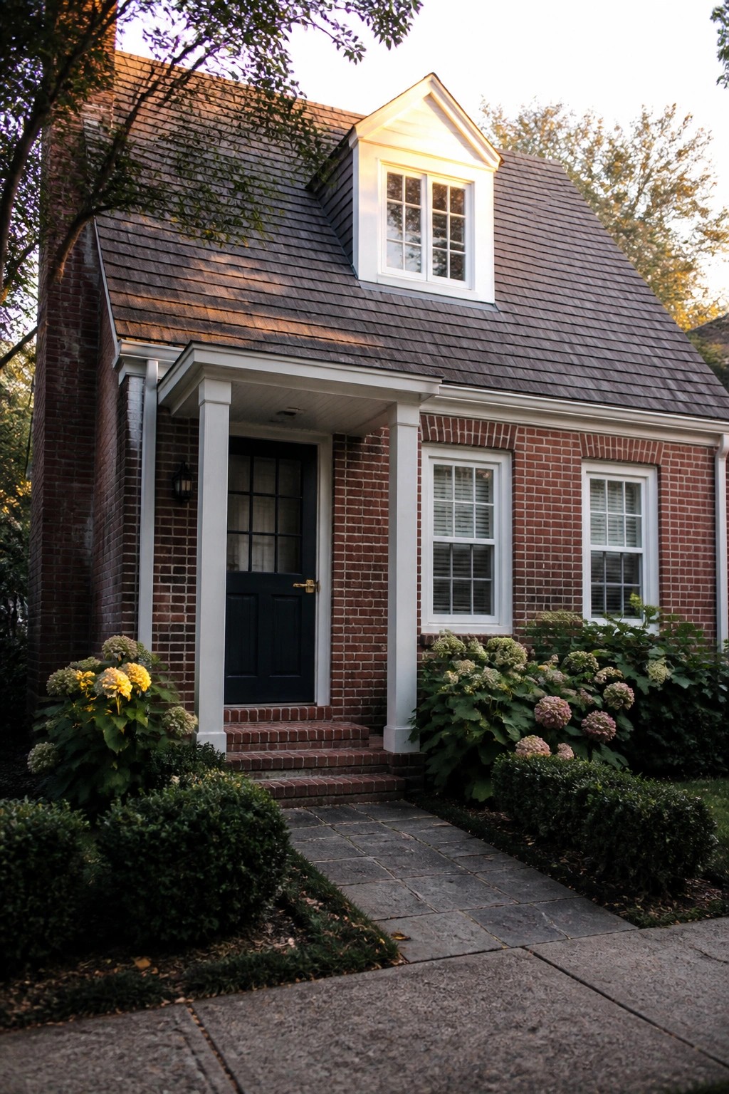 Brick house with dark door, white columns, dormer window, and blooming hydrangeas.