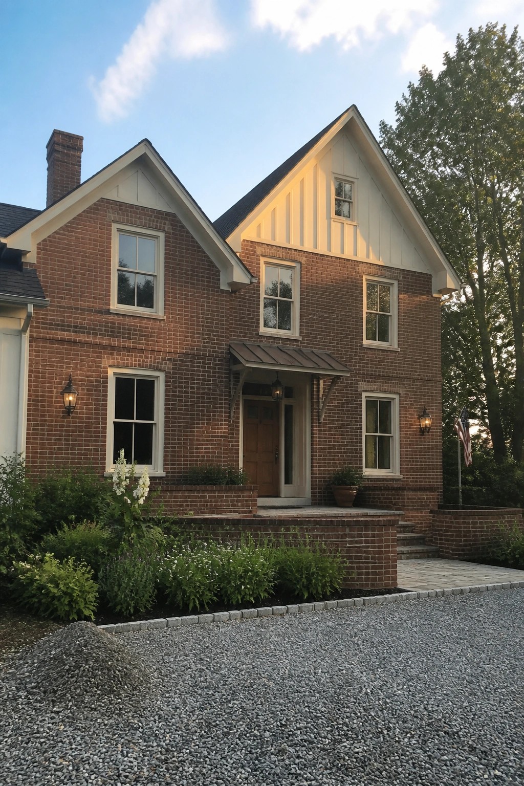 Two-story brick house with white gables, front porch, and American flag at dusk.