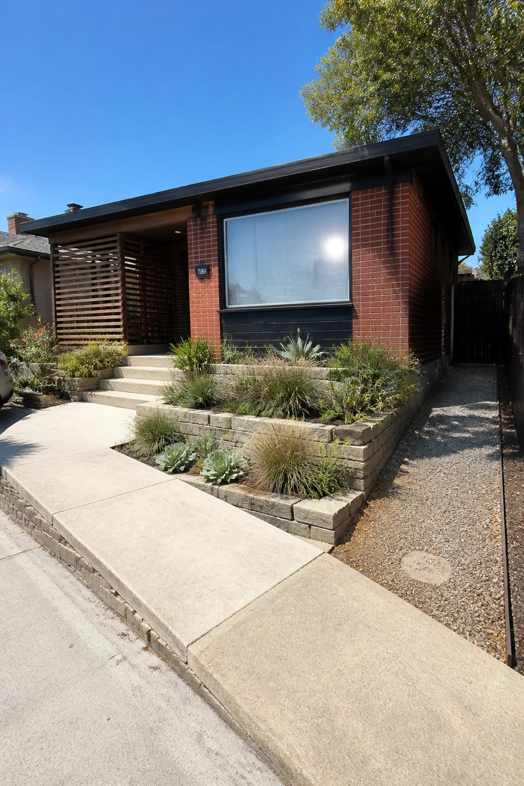Modern red brick house with large window, succulent garden, steps, and gravel path.