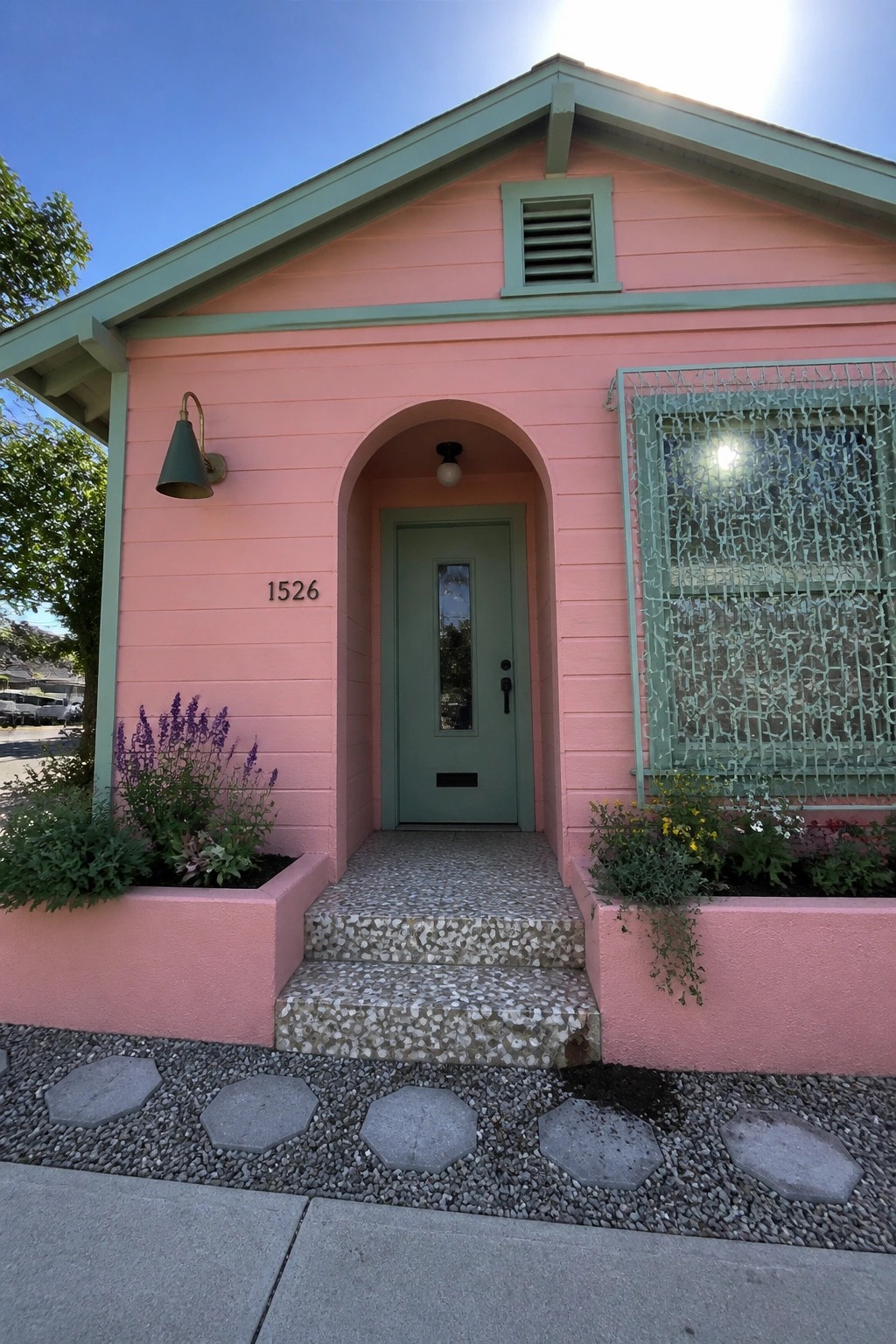 Pink house with green arched doorway, security gate on window, and flower planters.