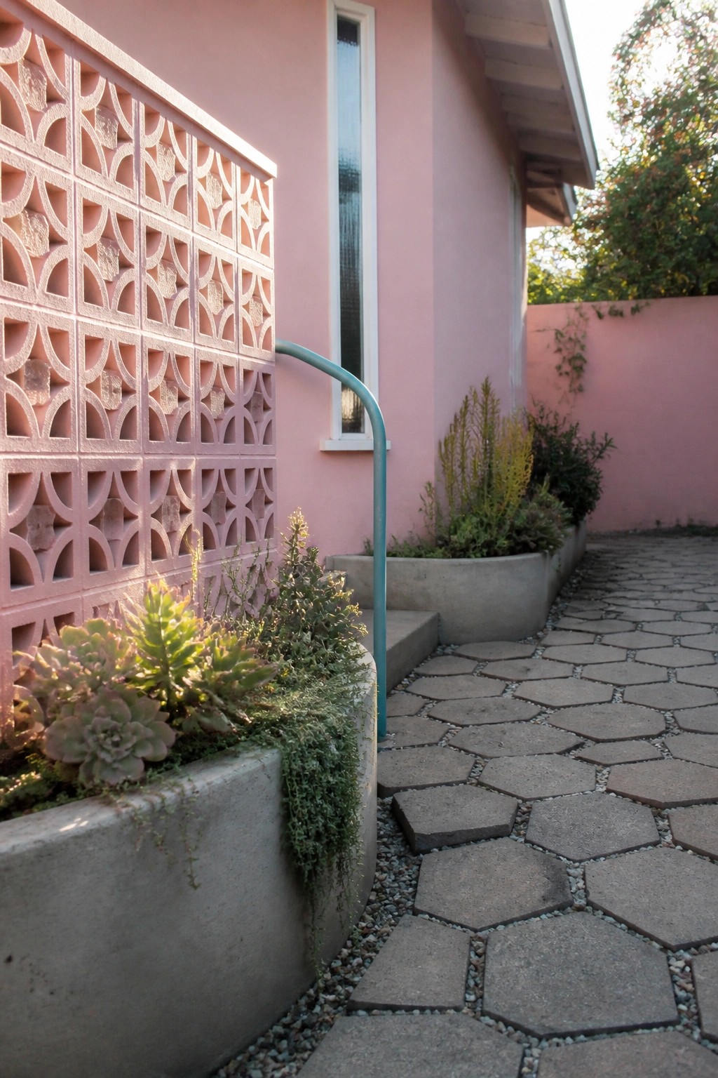 Pink stucco wall with breeze block screen, concrete planters of succulents, and hexagonal path.