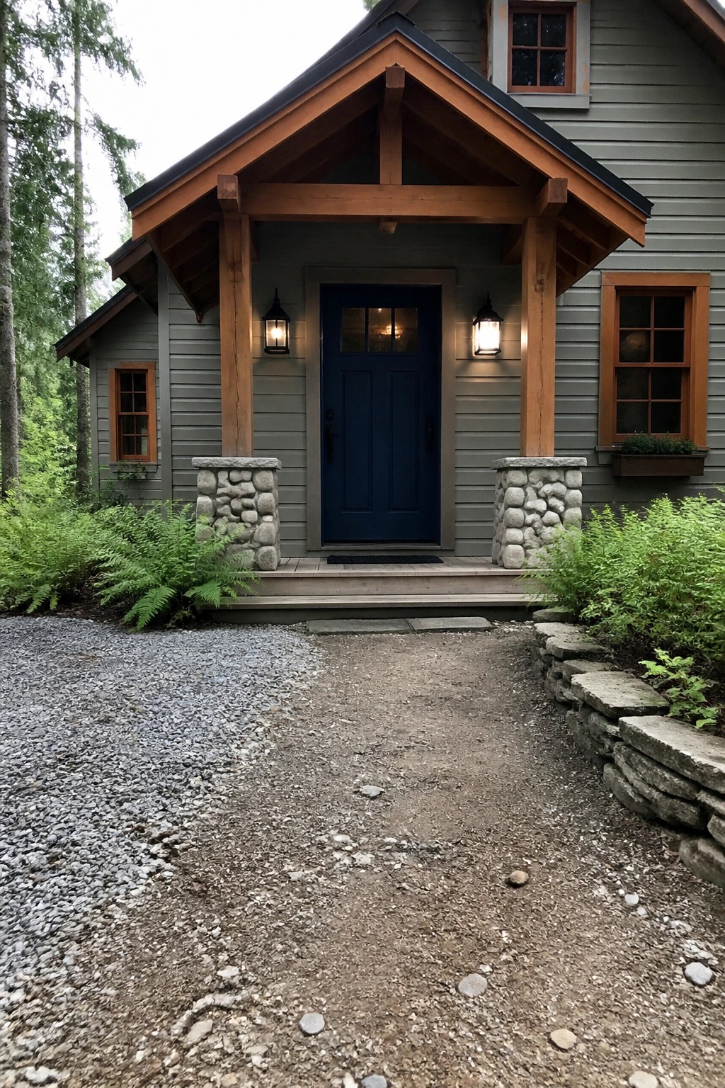 Gray house with blue door under wooden gable, stone pillars, lanterns, and gravel path.
