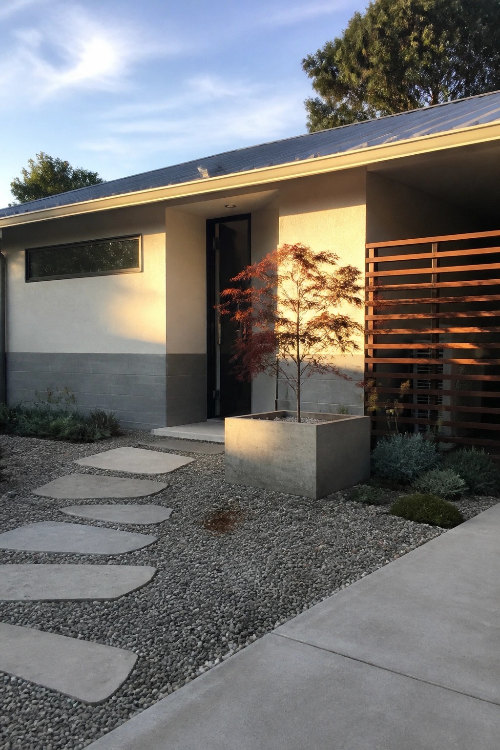 Modern house entrance with concrete planter, red maple tree, gravel path, and wooden screen