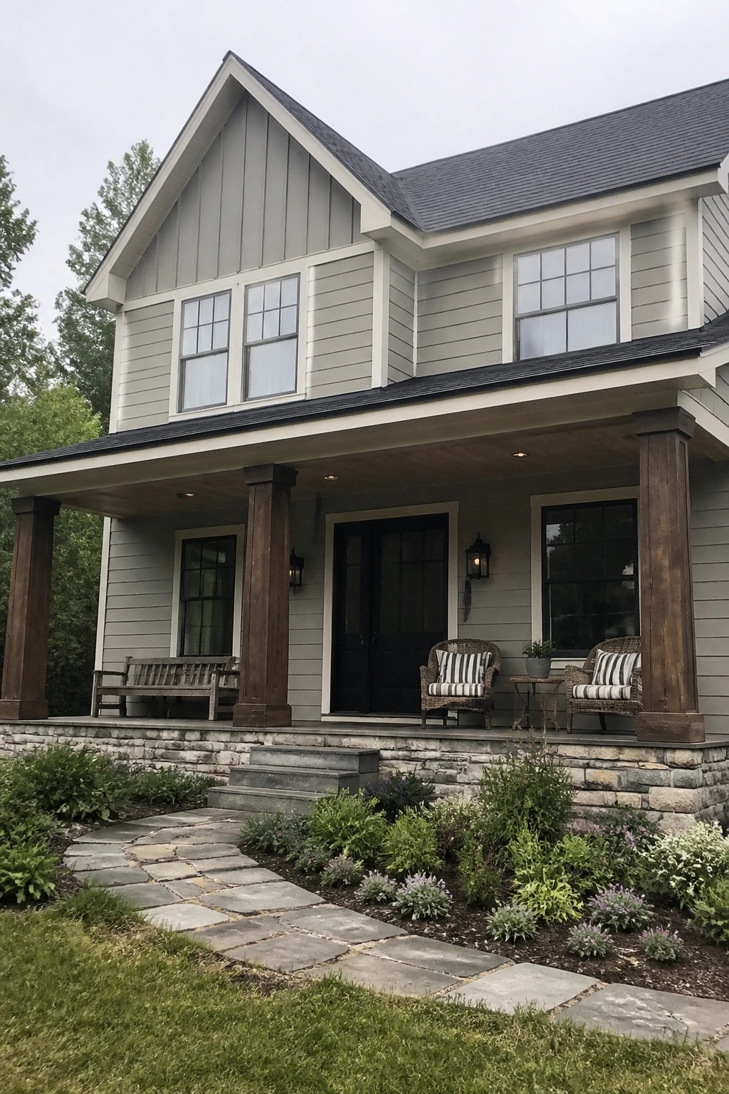 A two-story house with light gray siding, a dark roof, white trim, black windows and door, and a front porch with wooden columns on a stone foundation.