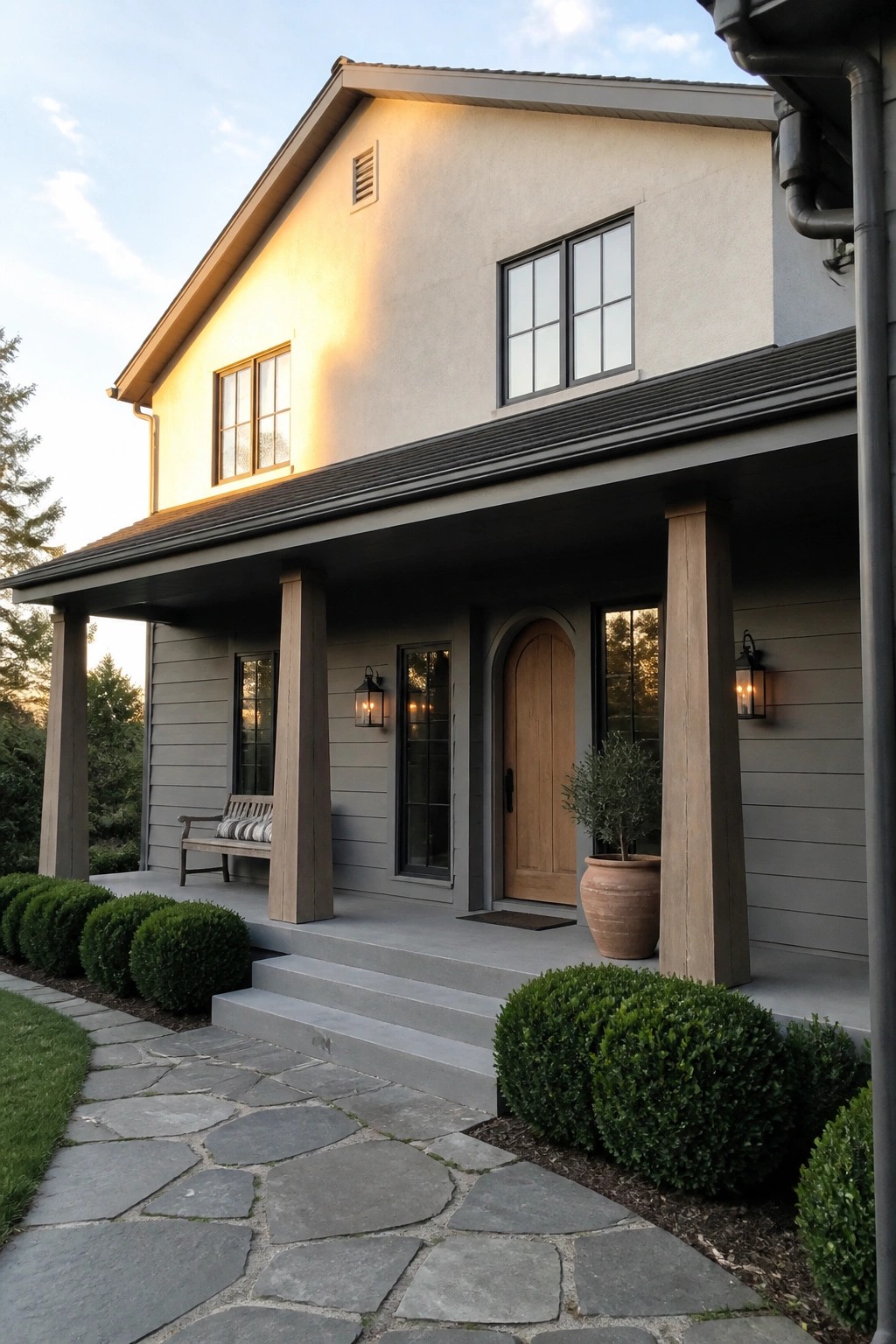 Modern gray house with wooden porch, arched door, stone path, and evening light