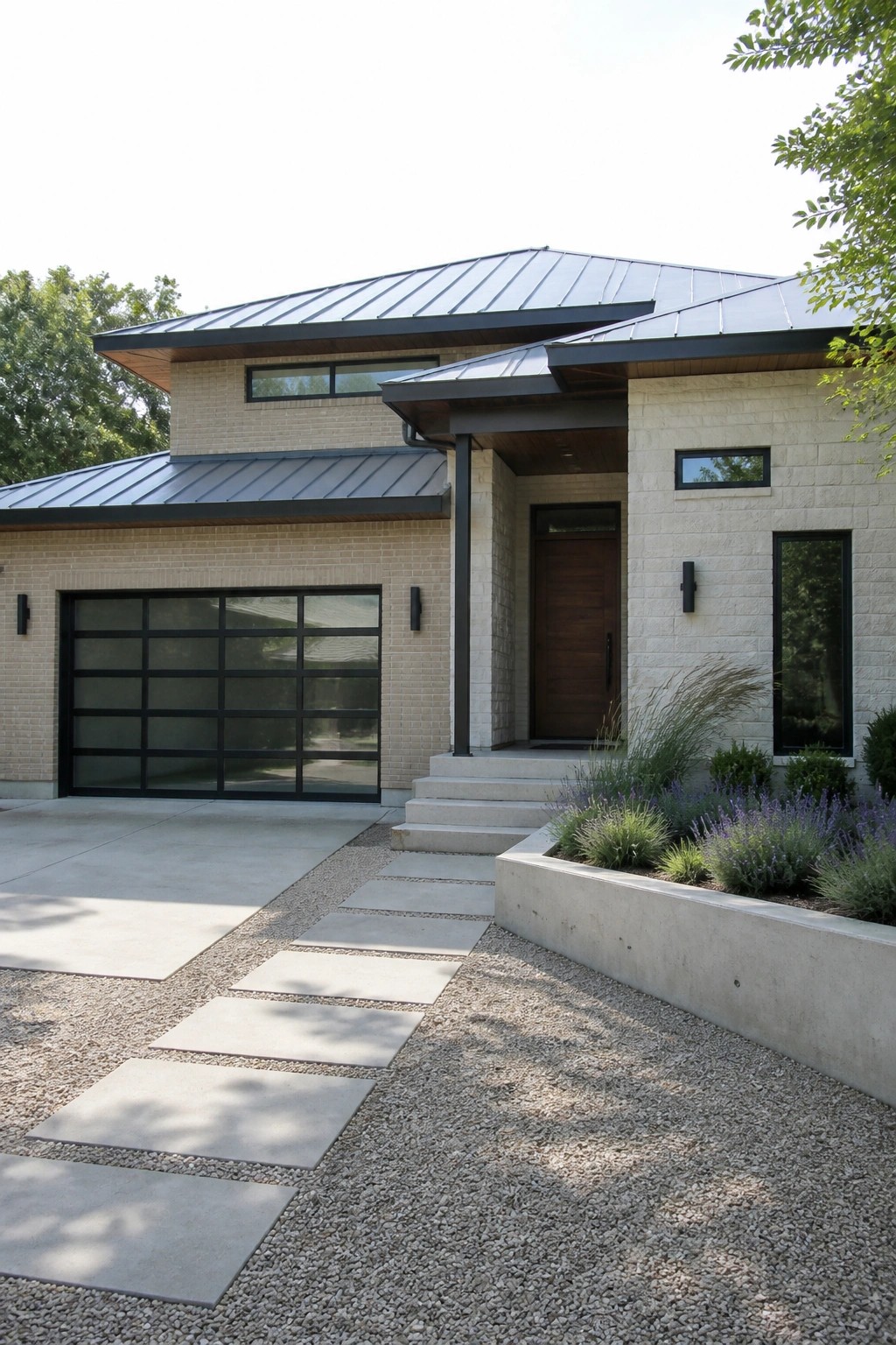 Modern beige brick home with dark metal roof, wooden door, and gravel paver path.