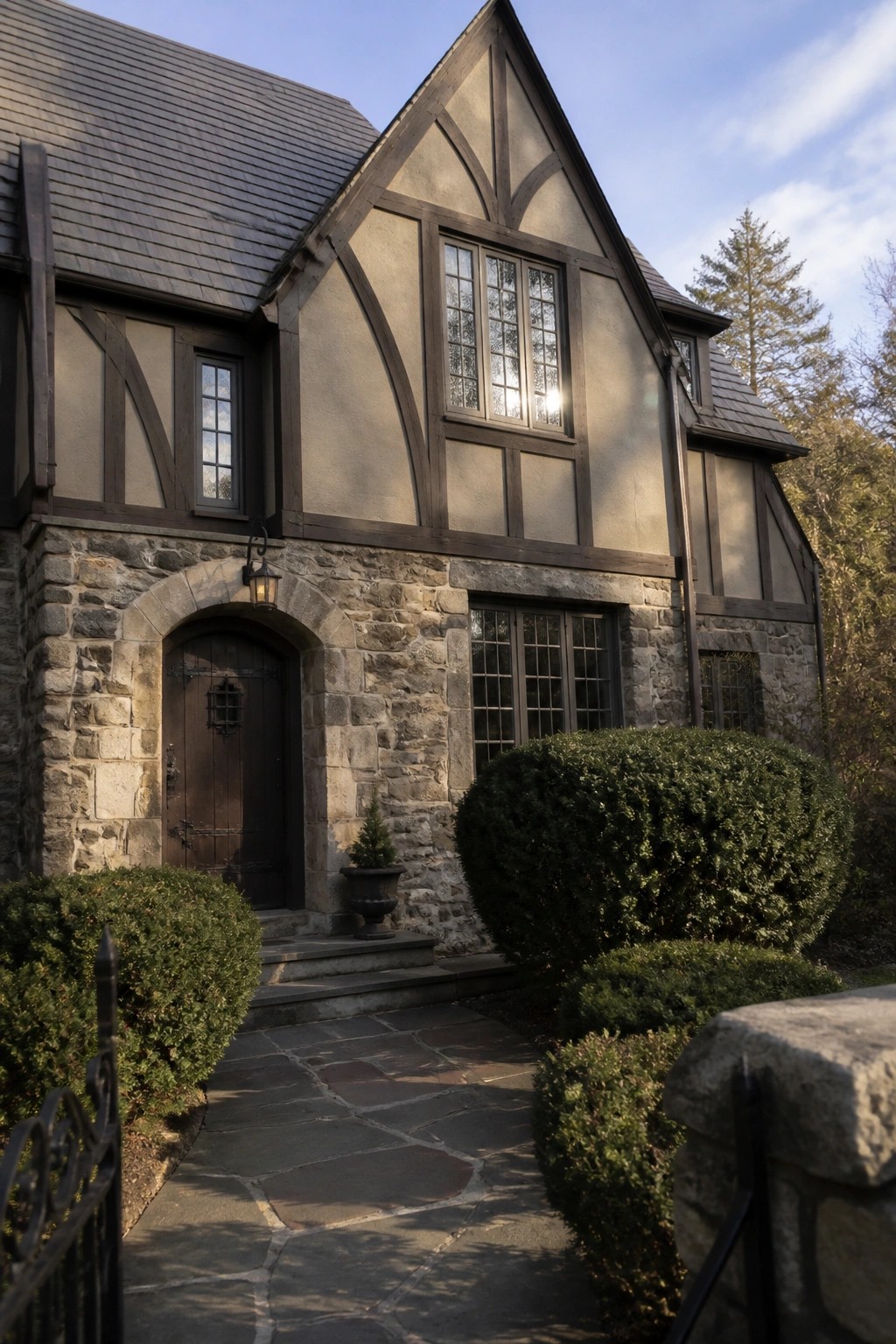 A Tudor-style house exterior with warm taupe stucco walls, dark timber framing, and a stone foundation.