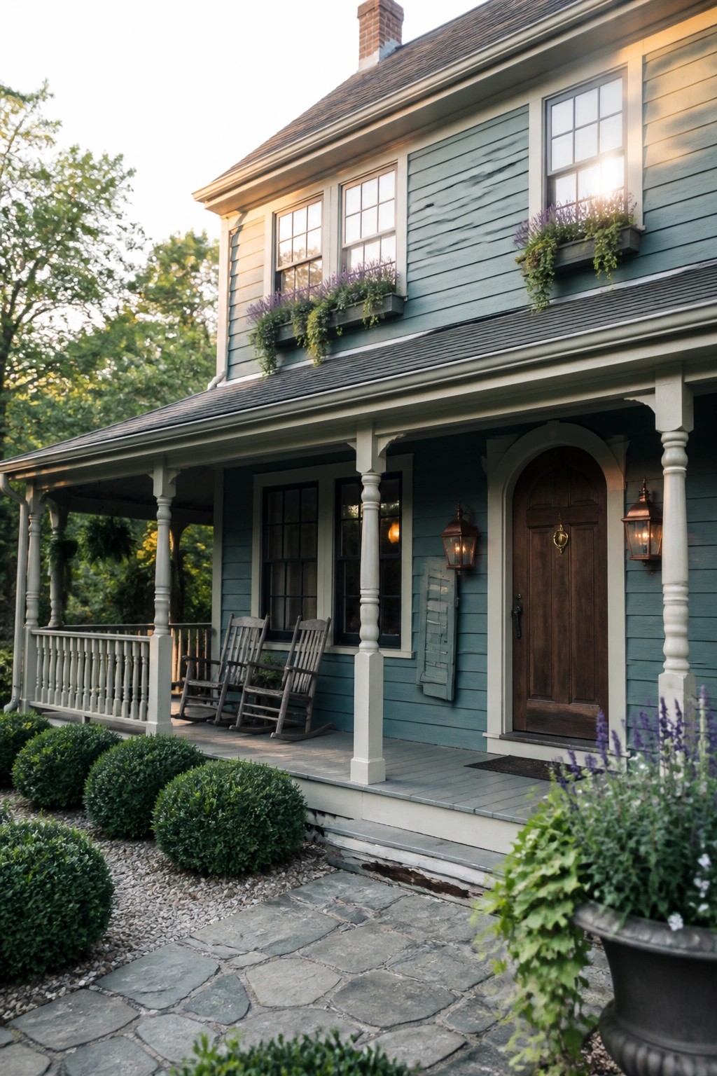 A two-story house with dusty teal wood siding, white trim, a covered front porch with rocking chairs, and a brown wooden door.