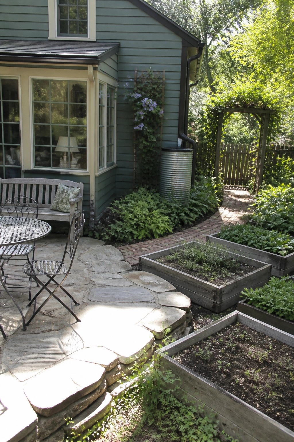 A dusty teal house exterior with raised wooden garden beds, a brick path, and a stone patio in the foreground.