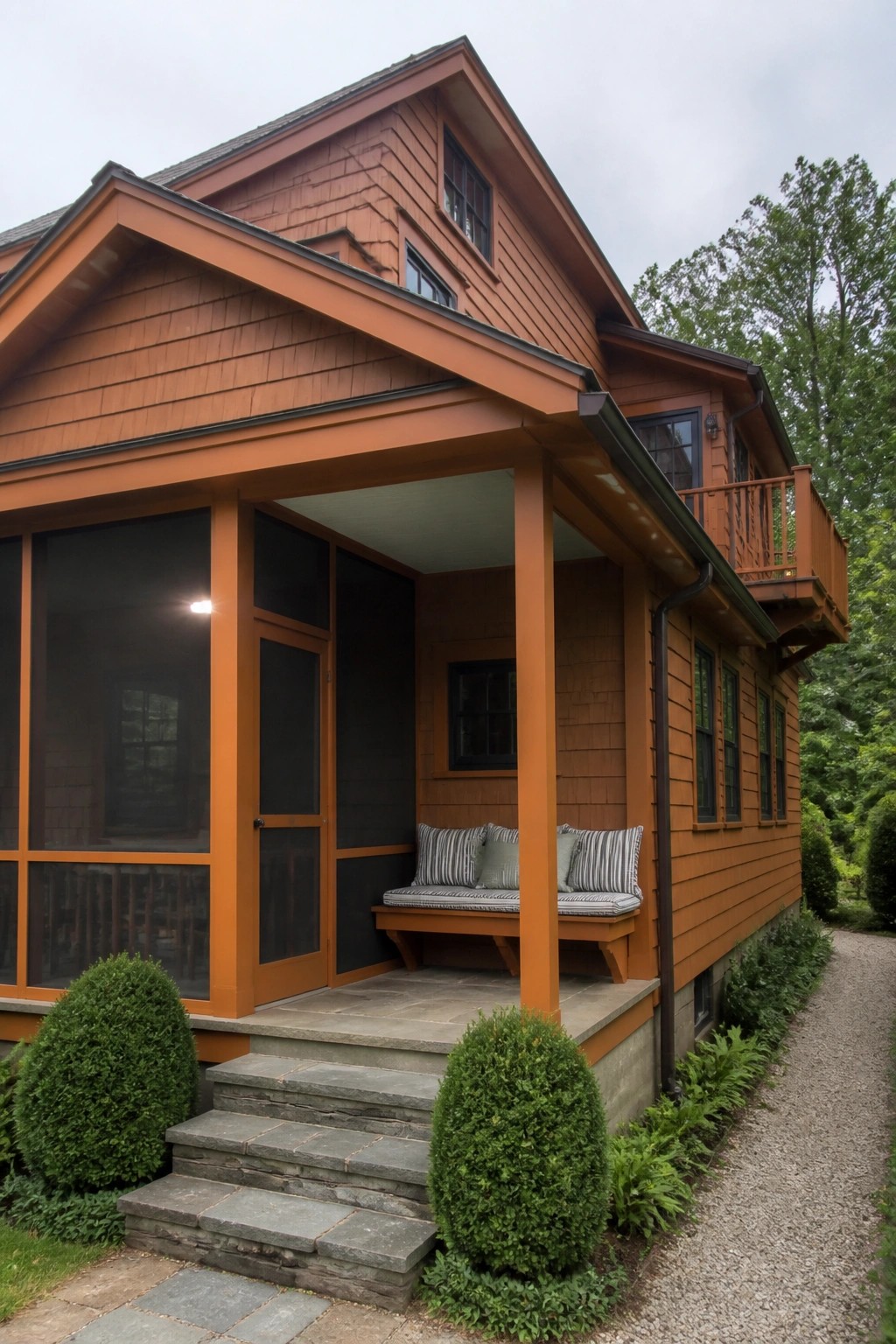 A two-story orange Craftsman house with shingle siding, a screened porch, wooden porch benches, stone steps, and a gravel side path.