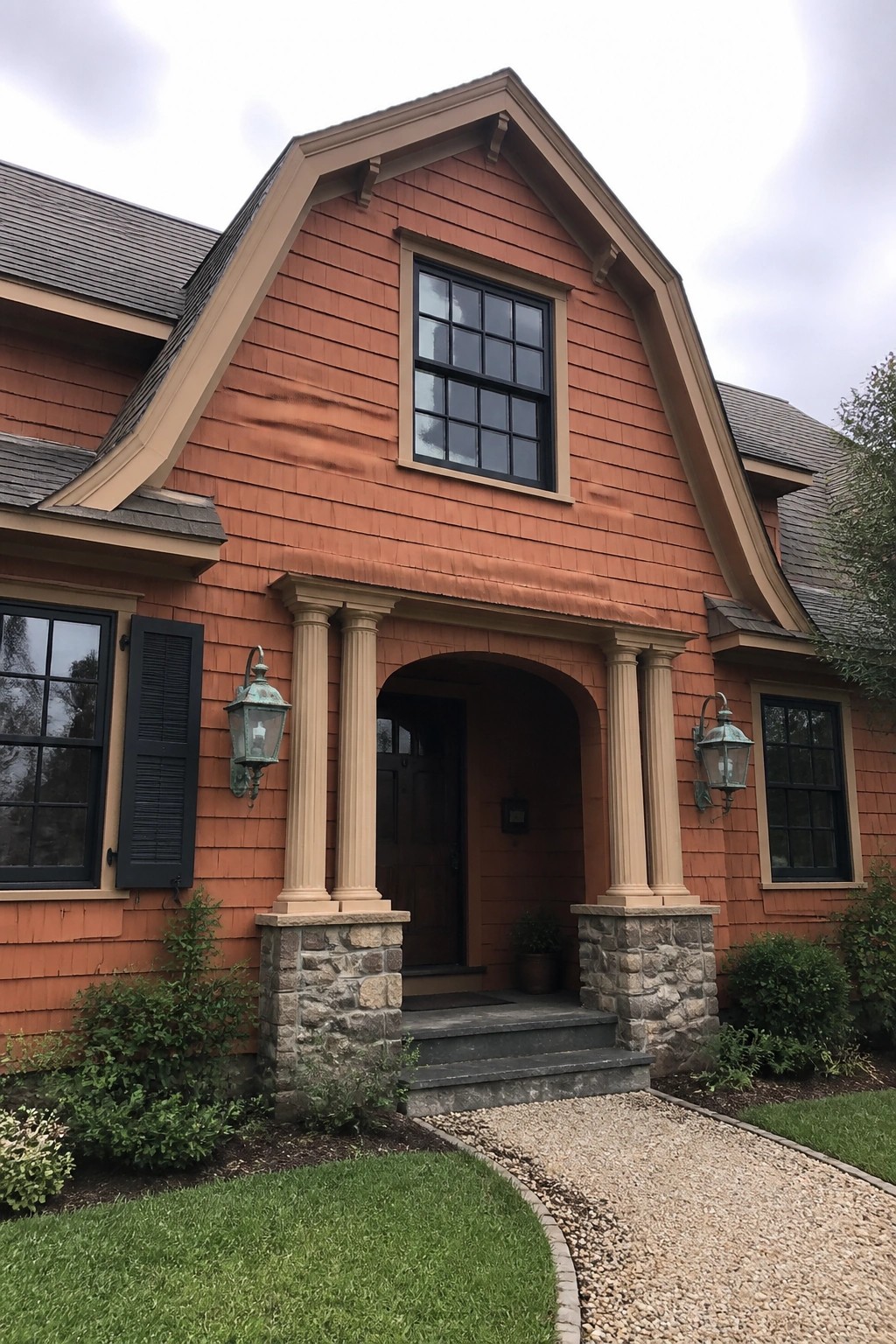 Red shingled house with arched columned entryway and gravel path to steps.