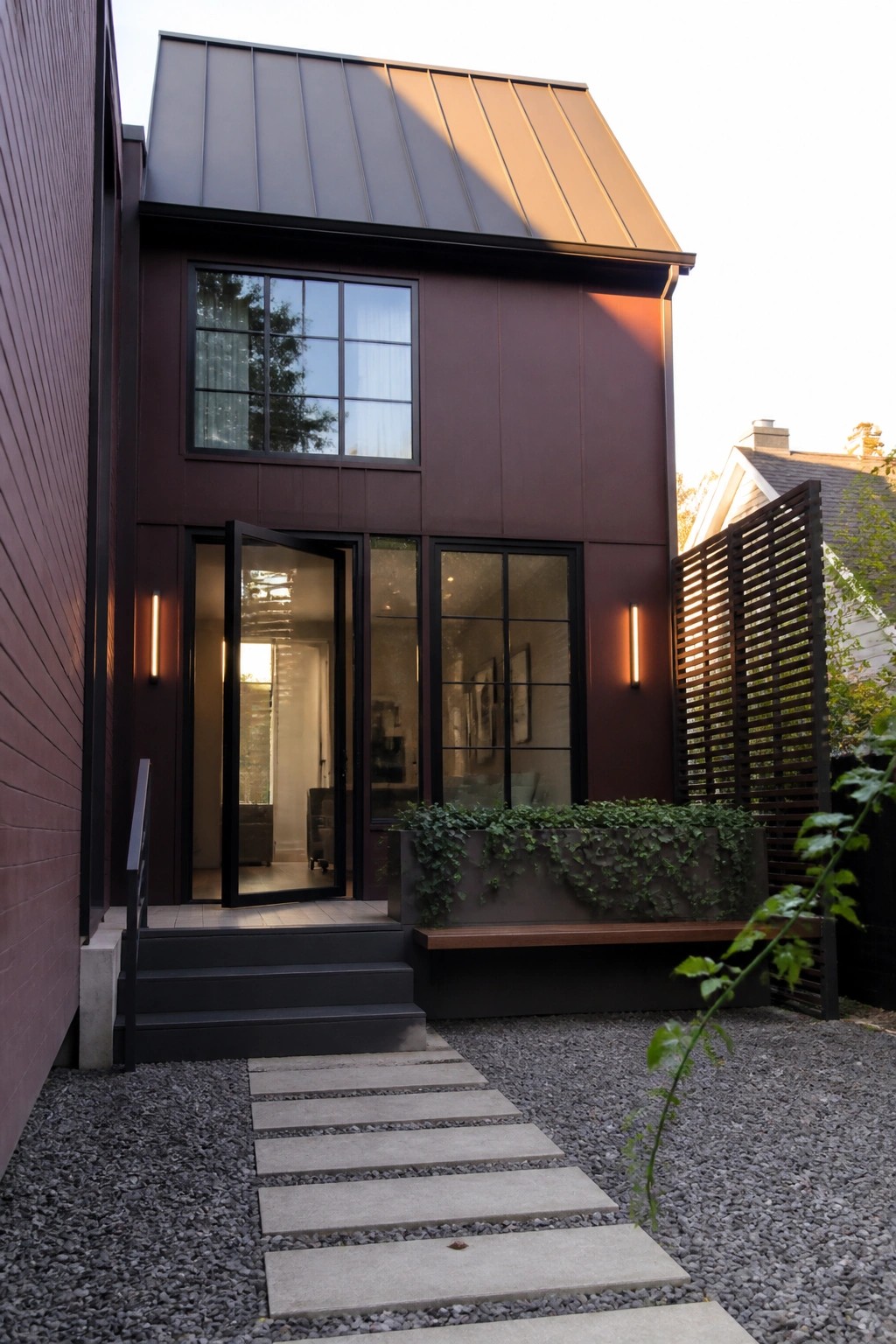 A two-story house with dark maroon siding, a charcoal metal roof, black-framed windows, and an open front door.