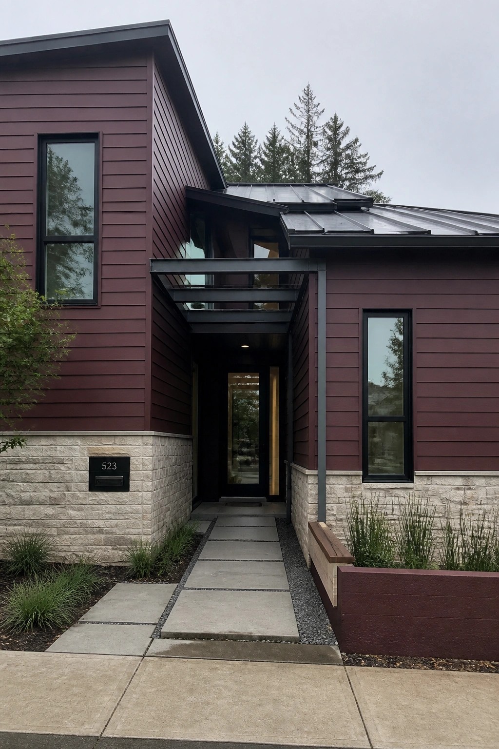 Modern maroon house with stone base, black door, and glass canopy entrance.
