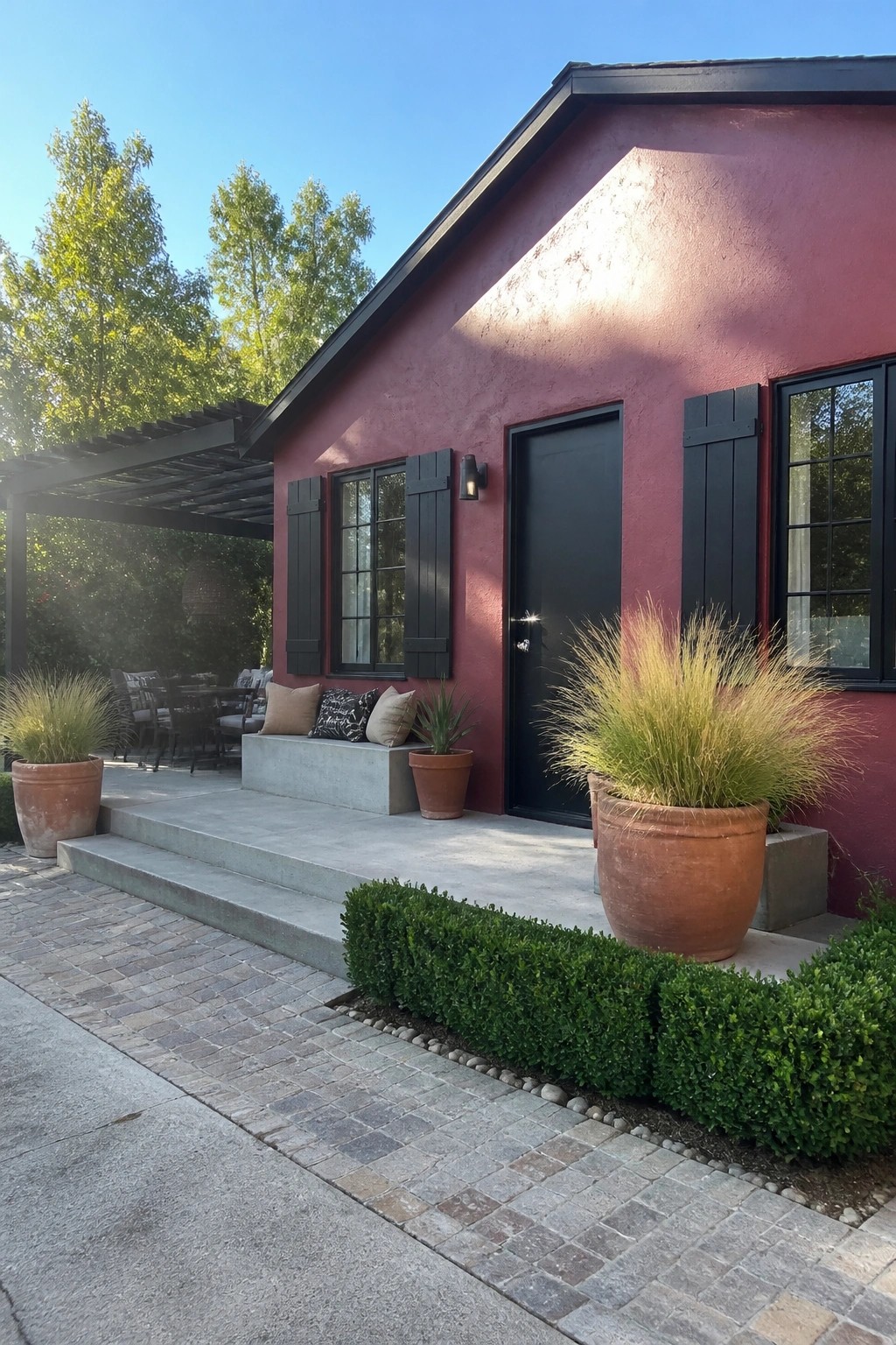 Red stucco house with black door, shutters, terracotta pots, and concrete steps